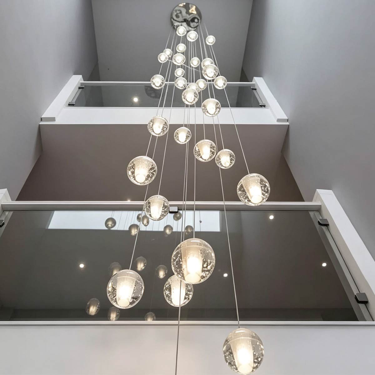 Looking straight up through open stairwell and modern glass railings at cascading crystal bubble ball pendant lights