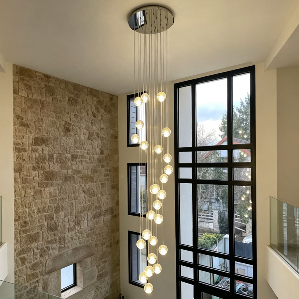 Grand 36-light spiral crystal bubble chandelier illuminating a luxury two-story foyer with stone accent wall and tall windows