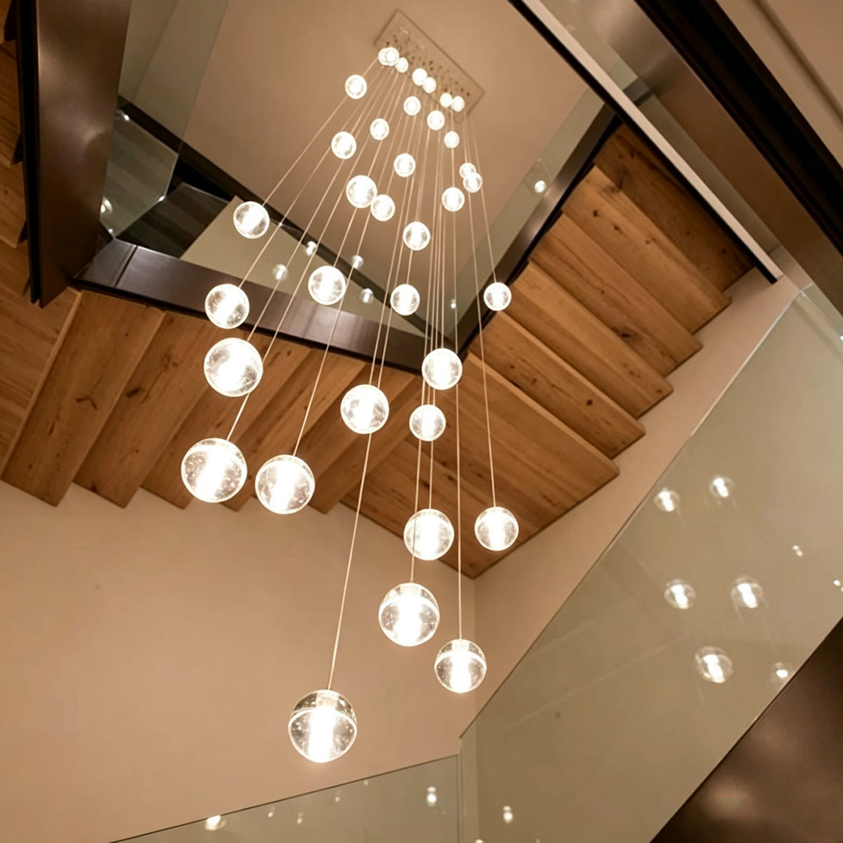 Looking up at cascading spiral crystal bubble pendant lights through open wooden stairwell
