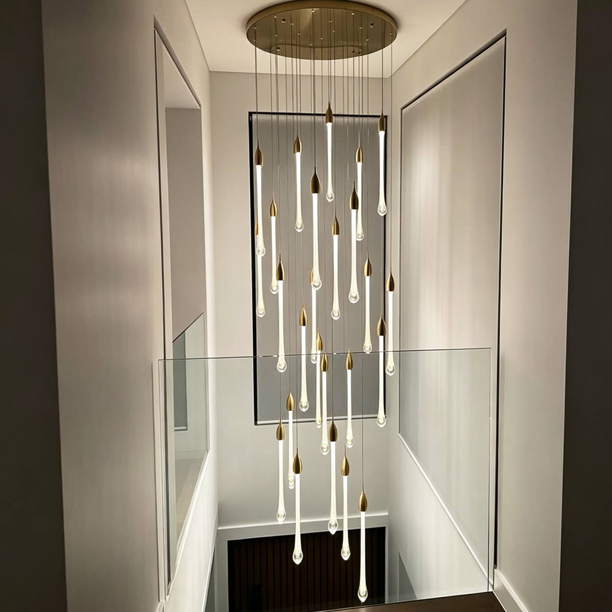 Vertical drop teardrop crystal chandelier illuminating contemporary two-story foyer and glass railing gallery