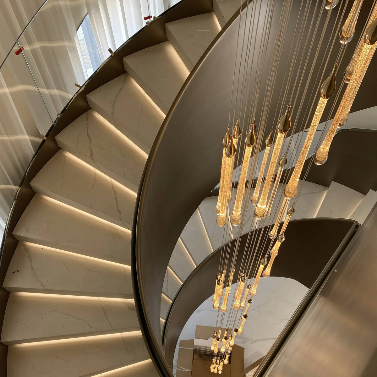 High angle view of multi-strand golden teardrop crystal pendant lights along curved marble staircase