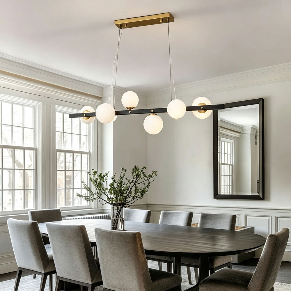 Black gold linear globe chandelier hanging over oval dining table, opal frosted glass globes, two‑tone metal pendant light for traditional classic dining room interior